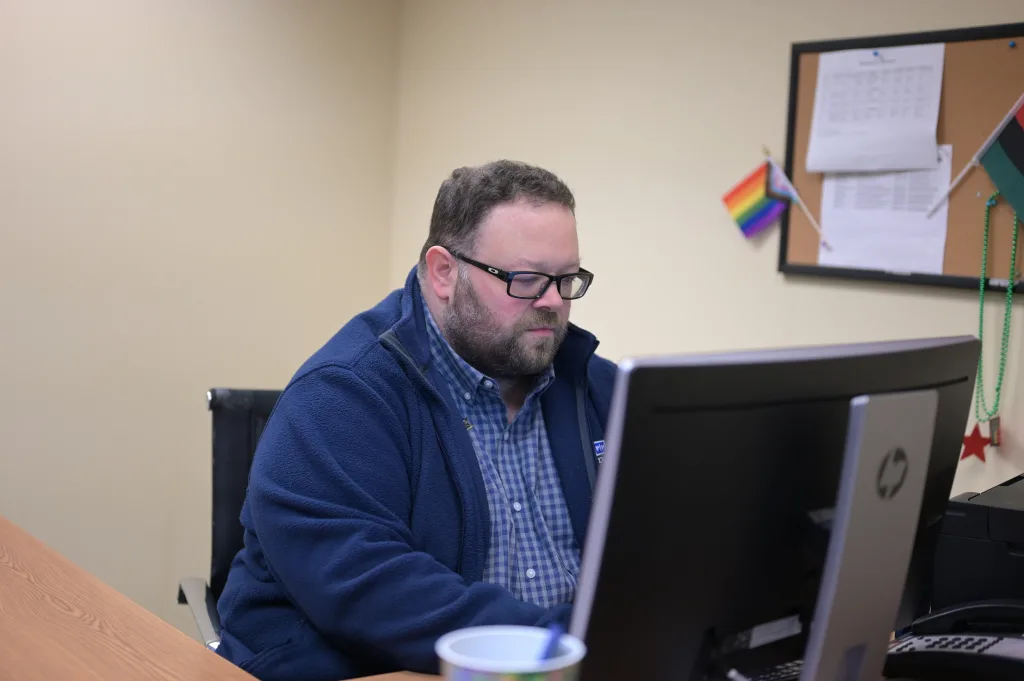 Clint Cox at computer with pride and juneteenth flags in background