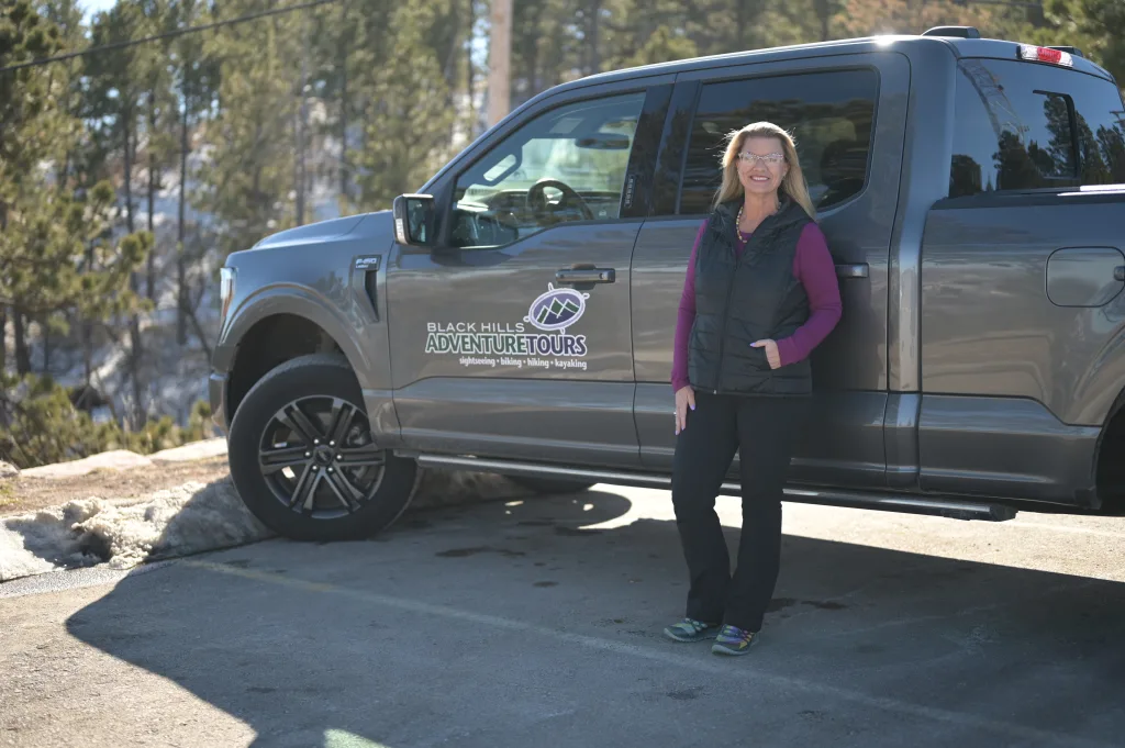 Carrie Gerlach stands in front of grey truck with Black Hills Adventure tours logo