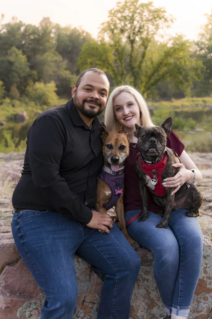 Couple sit on rock with two dogs on their laps.