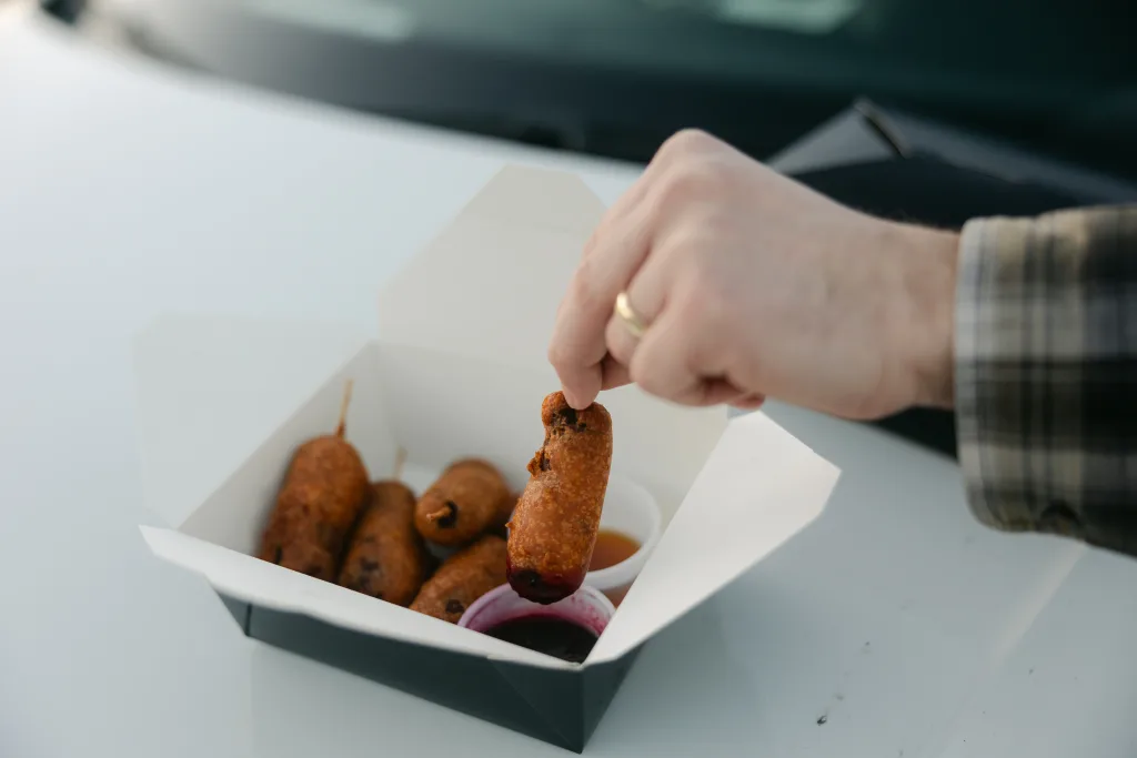 hand dipping food. a pork sausage link coated in pancake batter with berry medley syrup