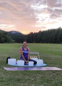 Monika Johncour sits in front of sunset surrounded by white sound bowls