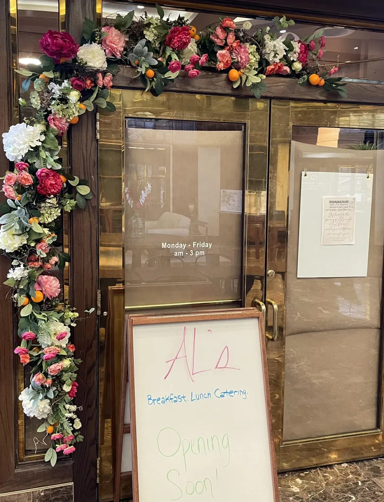 Door framed with flowers. Marker sign text reads Al's Breakfast. Lunch. Catering. Opening Soon!