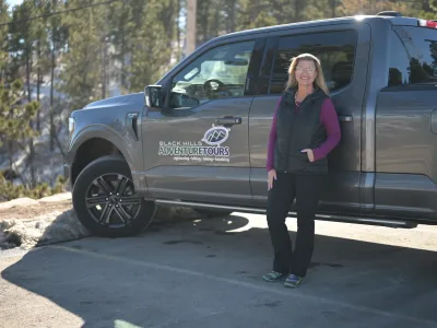 Carrie Gerlach stands in front of grey truck with Black Hills Adventure tours logo