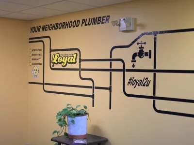 Brown wall with pipe design and words read Your Neighborhood Plumber, Loyal Plumbing logo, and #loyal2u