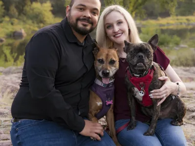 Couple sit on rock with two dogs on their laps.