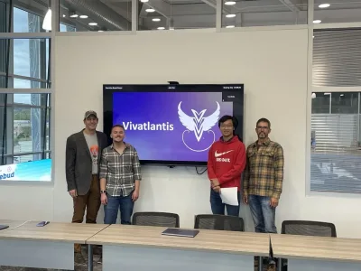 Group of four men pose in front of tv screen with vivatlantis logo